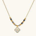 Gold-toned beaded necklace with grey stones and quatrefoil abalone shell pendant on cream background.